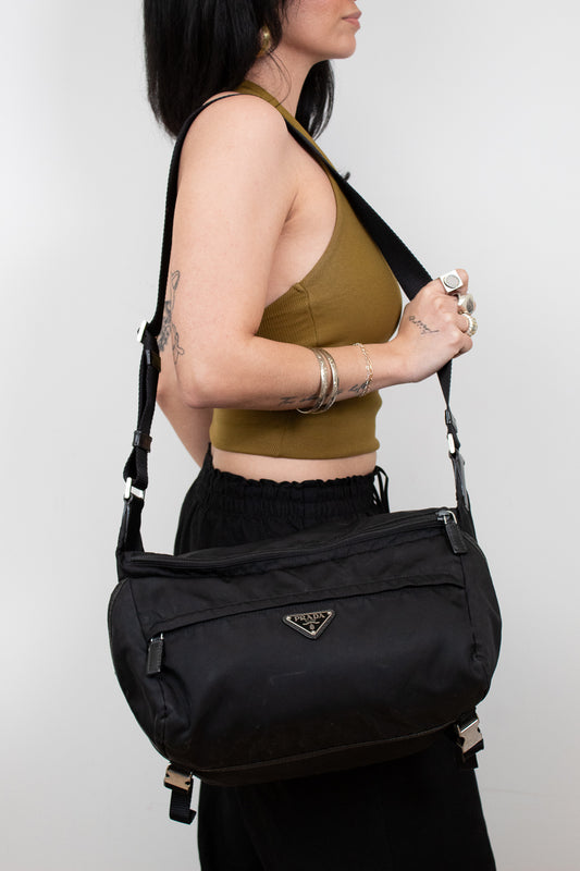 Person wearing a black Prada bag on a white background