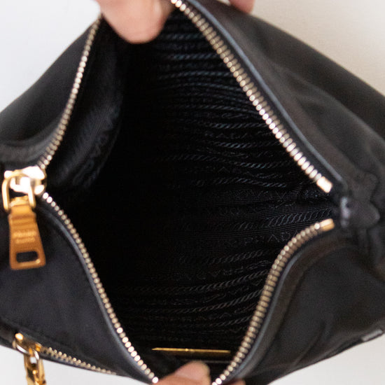 A close-up of a black nylon handbag being opened by two hands wearing silver rings, showing a black mesh interior and gold-tone zippers.