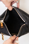 A close-up of a black nylon handbag being opened by two hands wearing silver rings, showing a black mesh interior and gold-tone zippers.