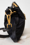 A black nylon shoulder bag with gold-tone hardware, featuring a drawstring top, leather trim, and a detachable shoulder strap, resting on a white marble surface.