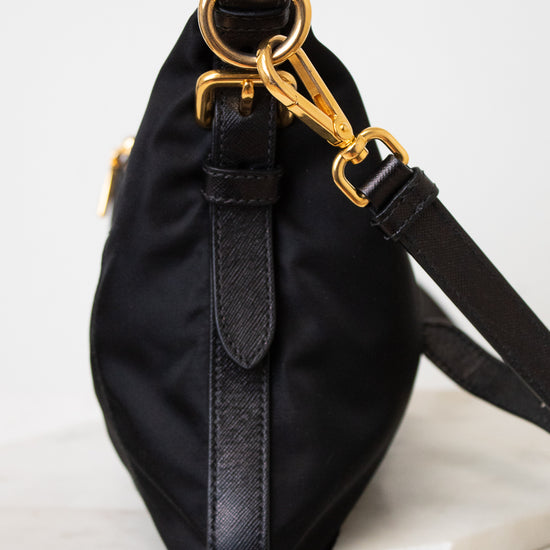 Side view of a black PRADA nylon shoulder bag featuring gold-tone ring hardware, a gold chain detail, stitched side panels , and a adjustable black shoulder strap.