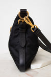 Side view of a black PRADA nylon shoulder bag featuring gold-tone ring hardware, a gold chain detail, stitched side panels , and a adjustable black shoulder strap.