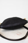 A black nylon crossbody bag with a black leather strap and gold-tone hardware, resting on a white marble surface against a white background.