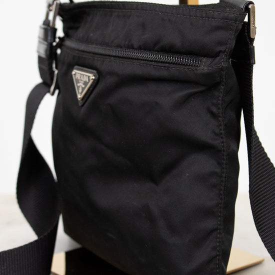 Black crossbody bag with a brand logo on a light background