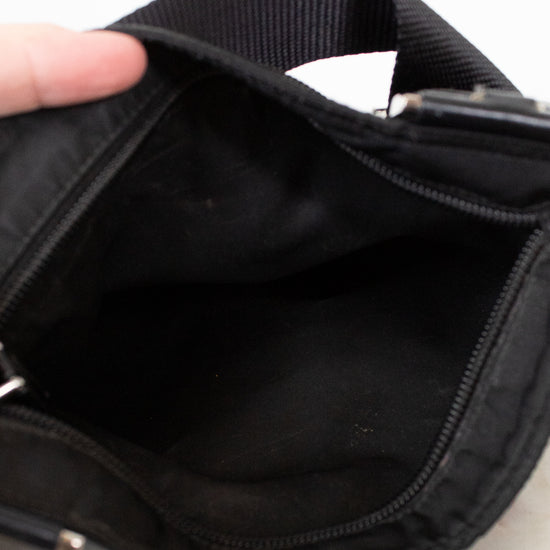 Close-up of a black bag with a hand holding it open on a light background
