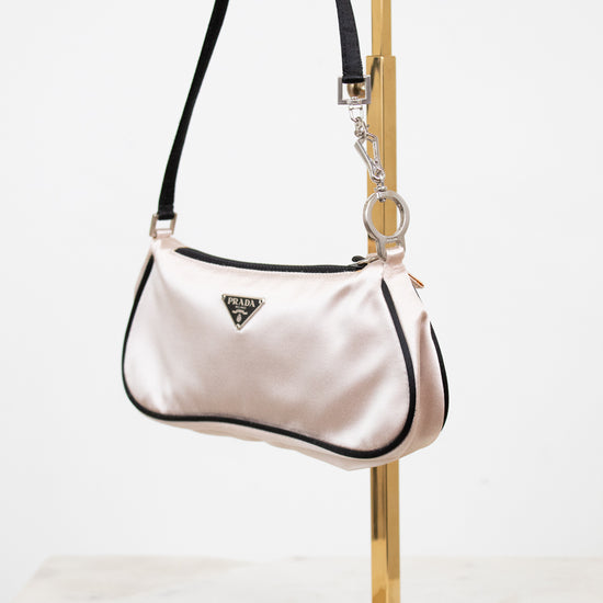 Light pink handbag with black accents on a gold stand against a white background