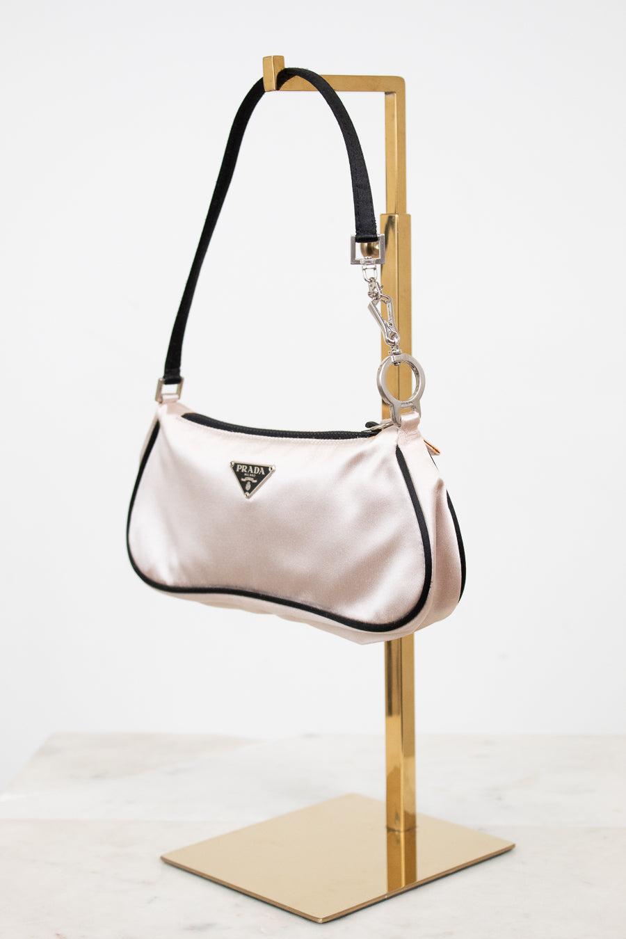 Light pink handbag with black accents on a gold stand against a white background