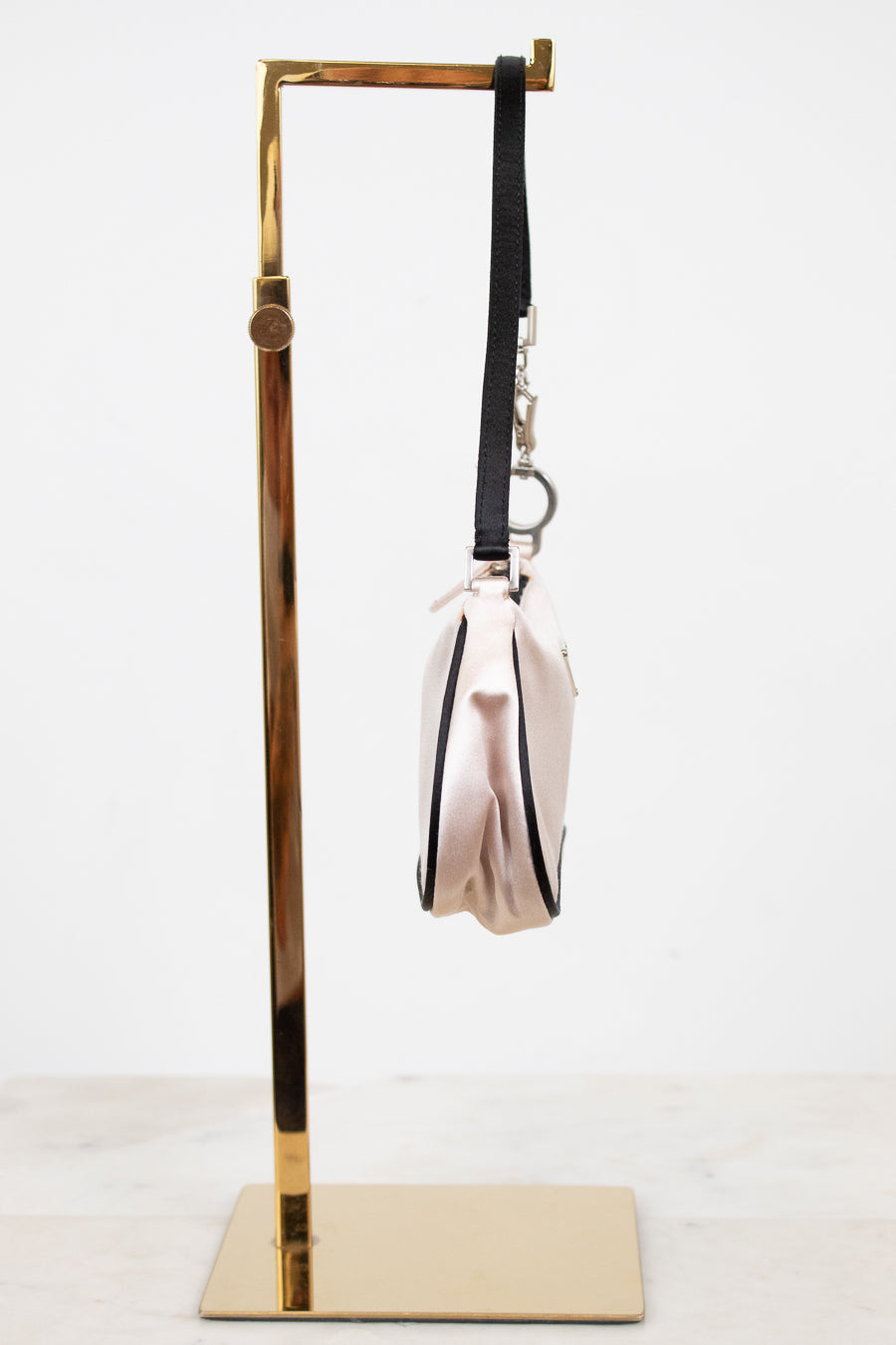 Side view of light pink bag with black strap on a white background