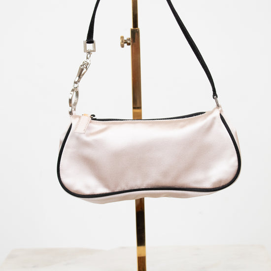 Light pink handbag on a gold stand against a white background