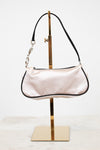 Light pink handbag on a gold stand against a white background