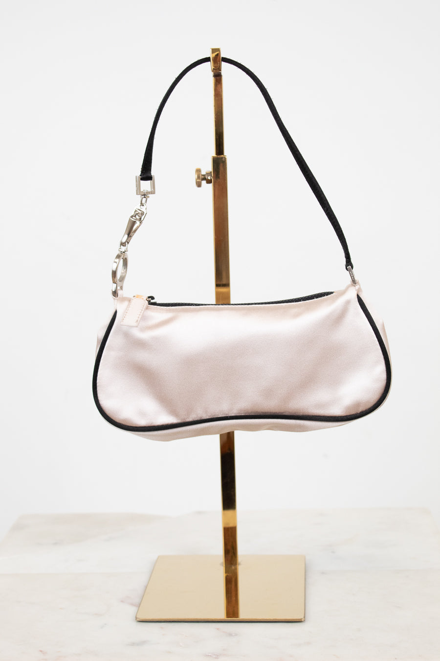 Light pink handbag on a gold stand against a white background