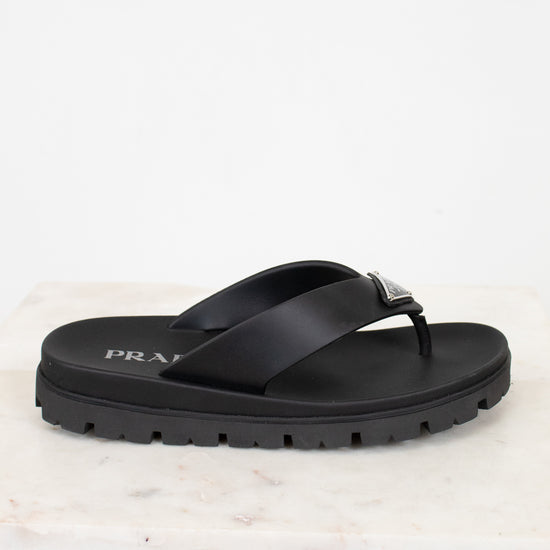 Black sandal with Prada logo on a light marble background