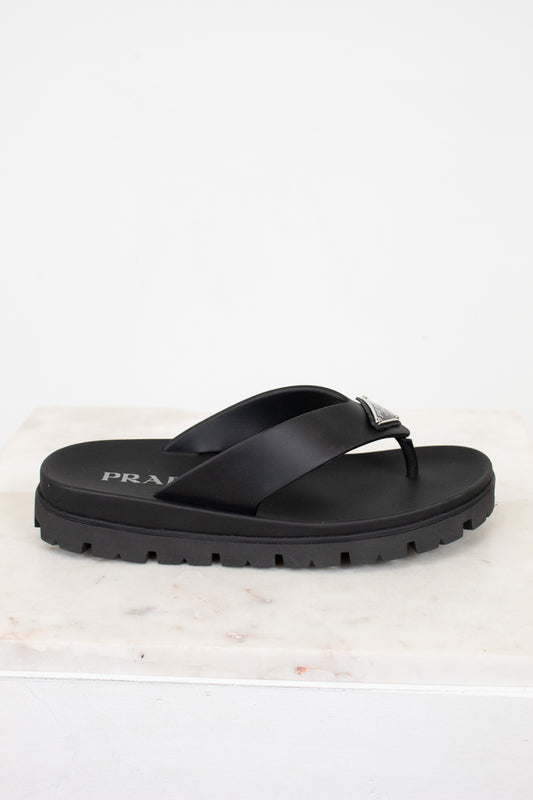 Black sandal with Prada logo on a light marble background