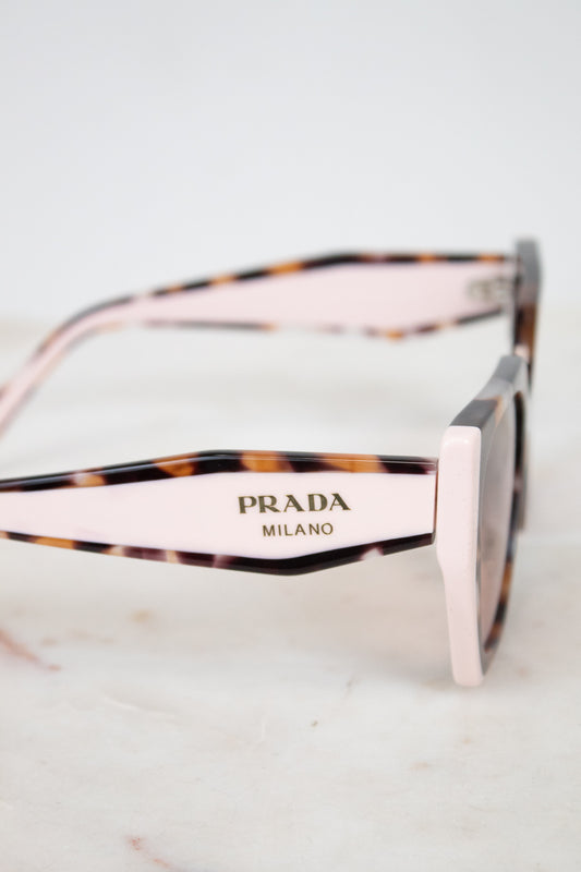 Prada Milano sunglasses with a light pink acetate front and temples, accented by a dark brown and black tortoiseshell pattern, resting on a light marble surface.