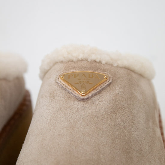 Close-up of beige suede and shearling slippers with a gold brand label on a white background