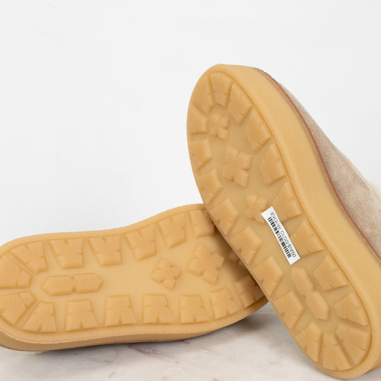 Close-up of bottoms of beige slippers with textured sole on a light background
