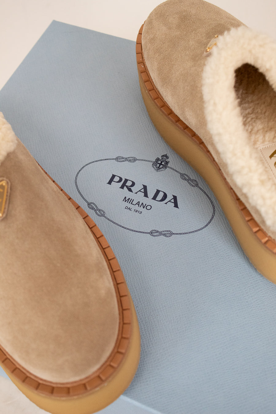 Beige slippers with Prada logo on a light blue box