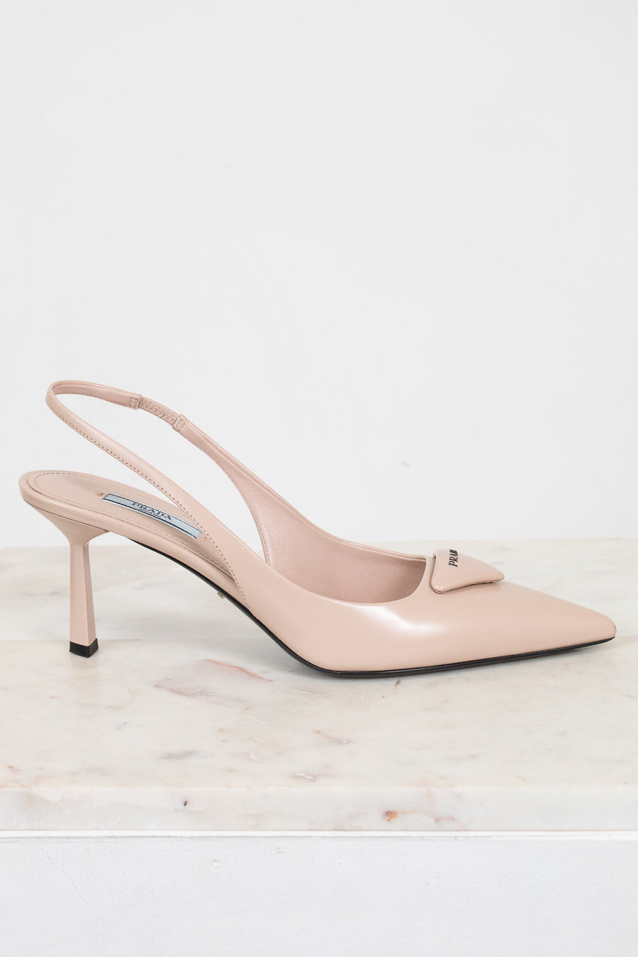 Nude high-heeled shoe on a light marble surface with a white background