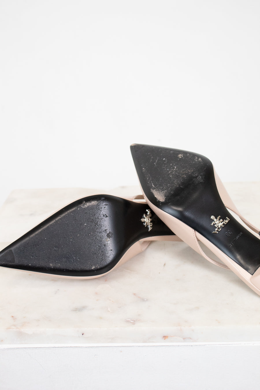 nude high-heeled shoes with black sole with gold accents on a marble surface