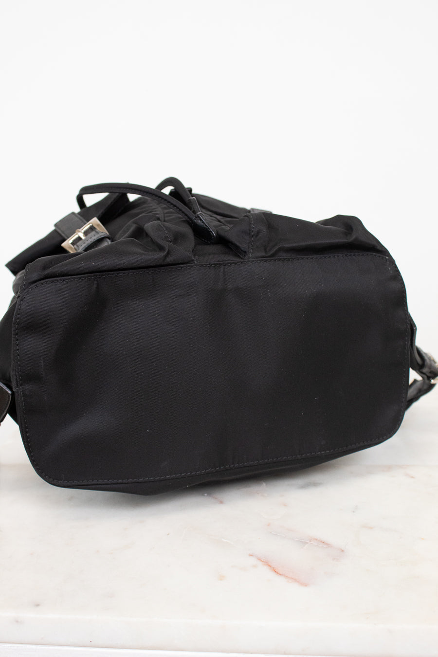 Bottom view of black nylon backpack against a plain background
