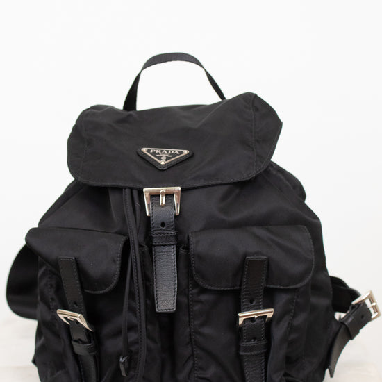 Black nylon backpack with exterior pocket and buckle details with top handle against a plain background