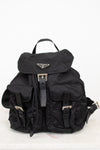 Black nylon backpack with exterior pocket and buckle details with top handle against a plain background