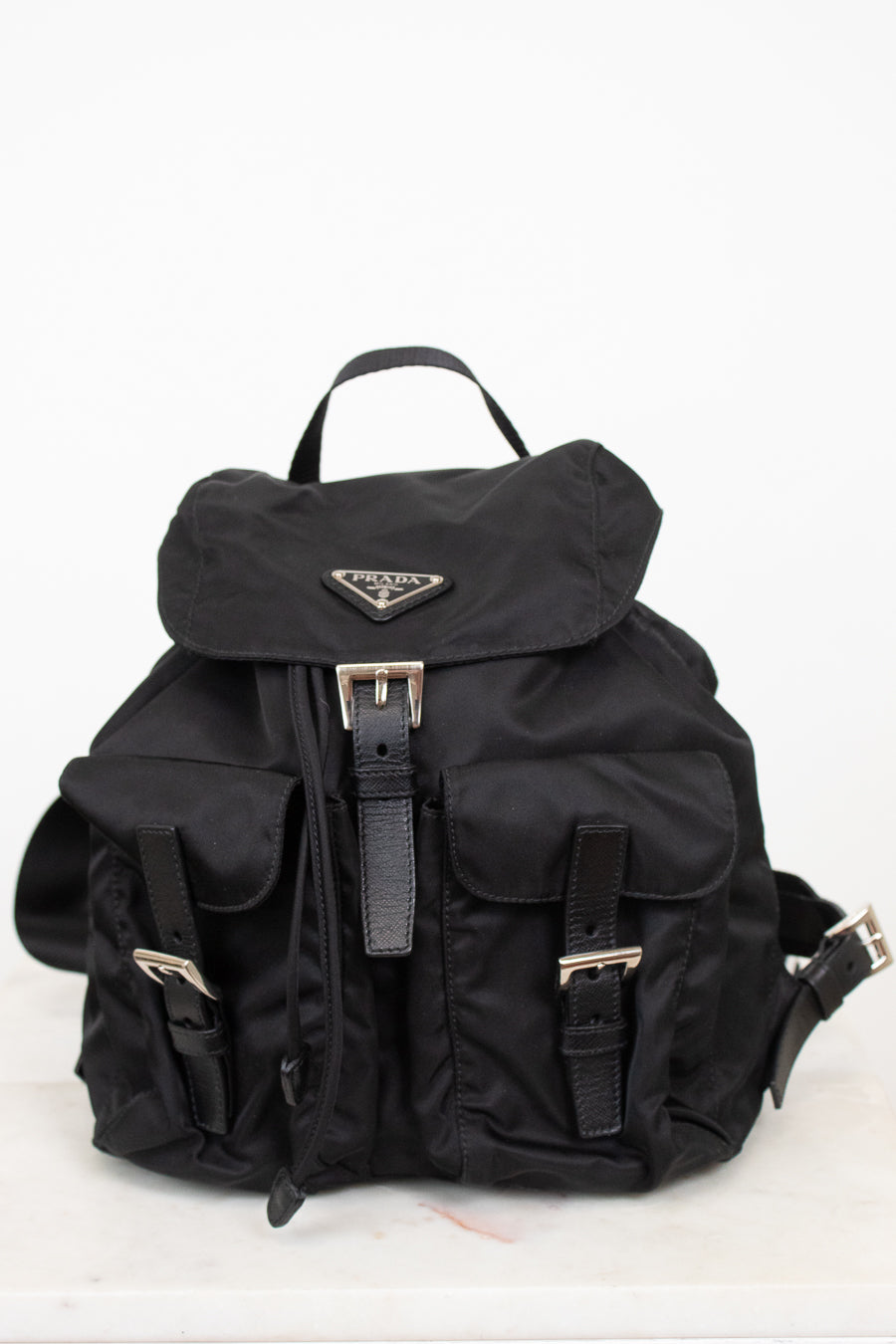 Black nylon backpack with exterior pocket and buckle details with top handle against a plain background