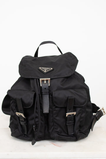 Black nylon backpack with exterior pocket and buckle details with top handle against a plain background