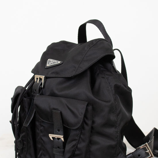 Side view of black nylon 'PRADA' backpack against a plain background