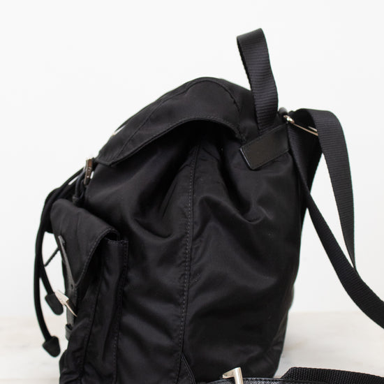 Side view of black nylon backpack against a plain background