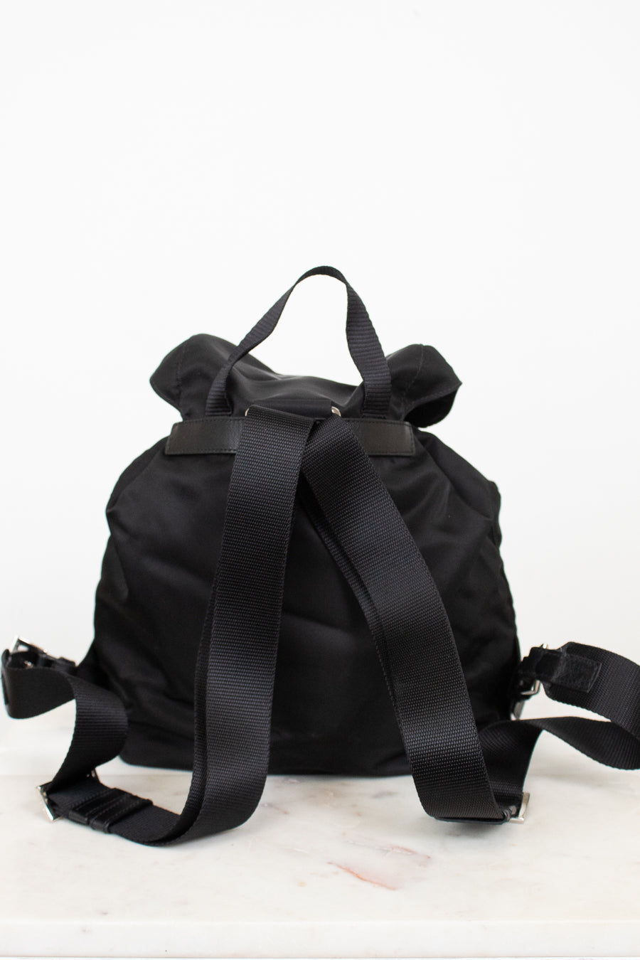 Back view of black nylon backpack showing adjustable straps and top handle displayed against a plain background