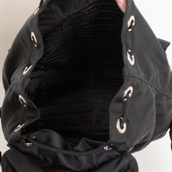 Hand holding open black nylon back showing drawstring closure and dark lined interior