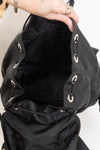Hand holding open black nylon back showing drawstring closure and dark lined interior