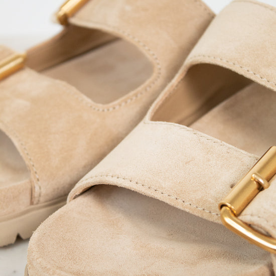 Beige sandals with gold buckles on a light gray background