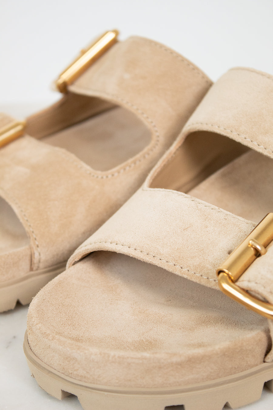 Beige sandals with gold buckles on a light gray background
