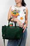Person holding a green handbag wearing a colorful sleeveless top and jeans against a plain background