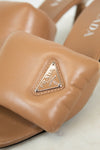 Close-up of tan leather sandals with Prada logo on a light background
