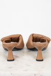 A pair of tan leather mule heels with a unique flared block heel and open toe, shown from the back on a white marble surface against a white background.