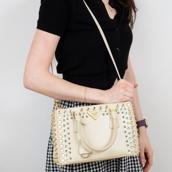 Woman holding a beige handbag with decorative elements against a plain background