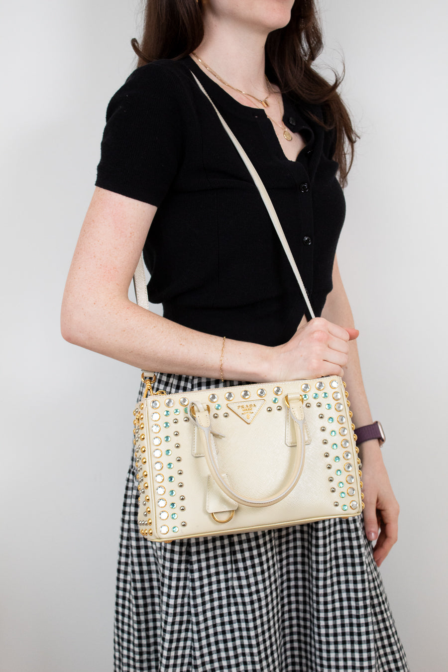 Woman holding a beige handbag with decorative elements against a plain background