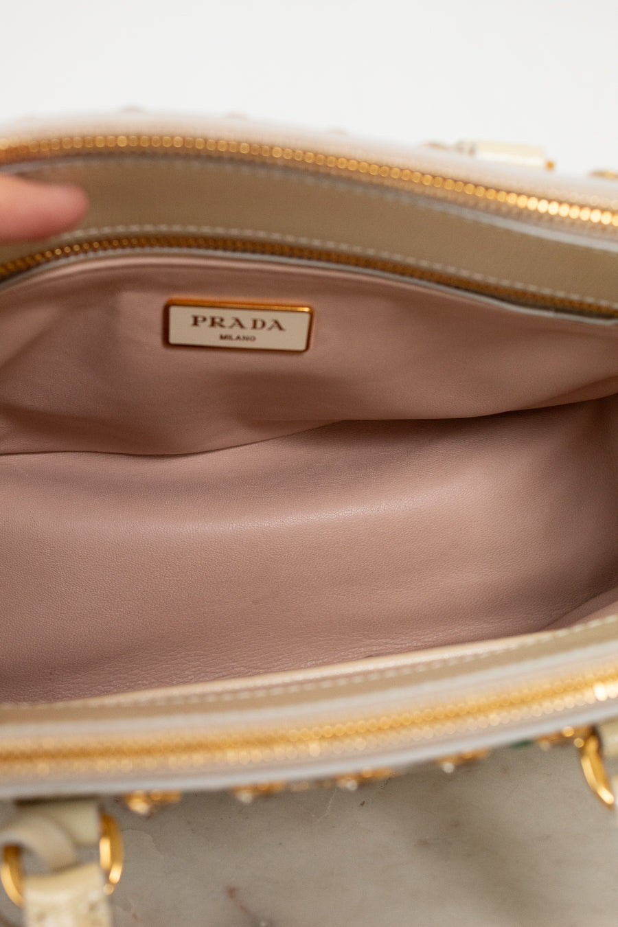 Close-up of a Prada handbag with a gold zipper and beige interior.