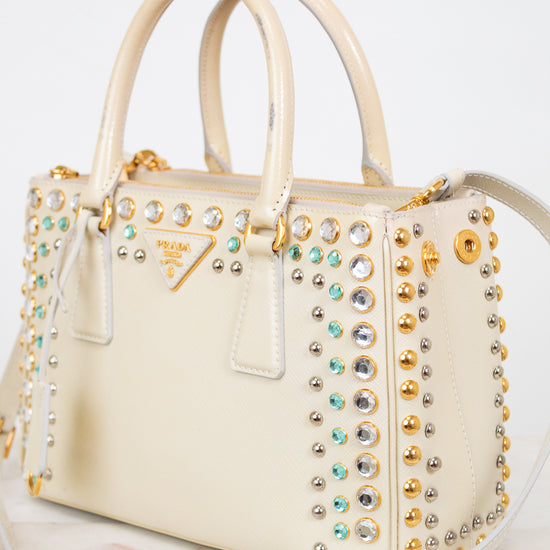 Beige handbag with gold and silver studded details on a white background
