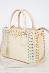 Beige handbag with gold and silver studded details on a white background