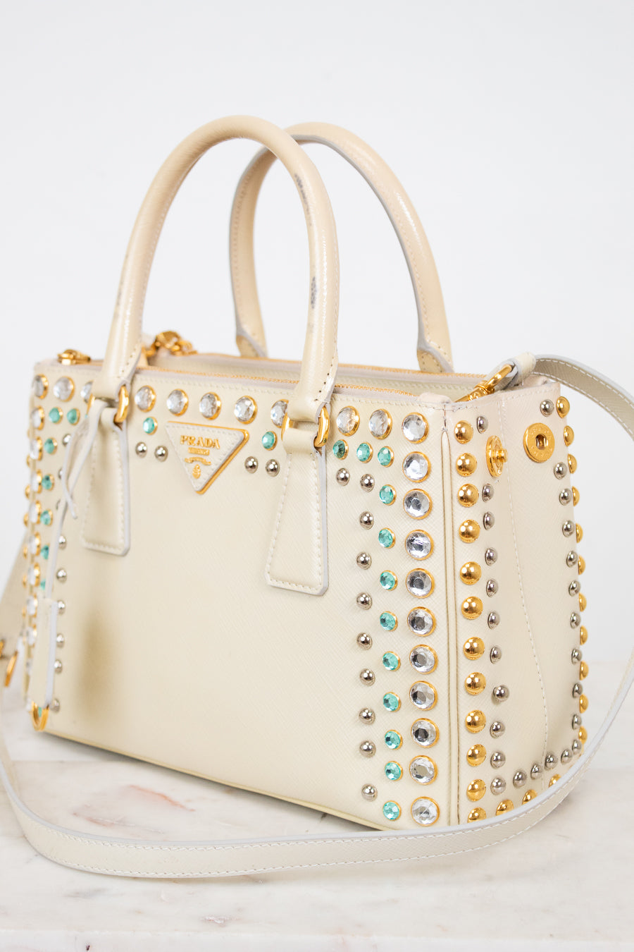 Beige handbag with gold and silver studded details on a white background