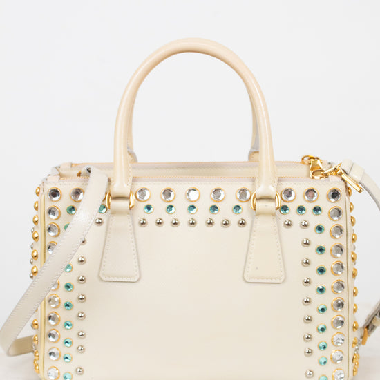 Cream-colored handbag with gold and multi-color gemstone embellishments on a light gray background