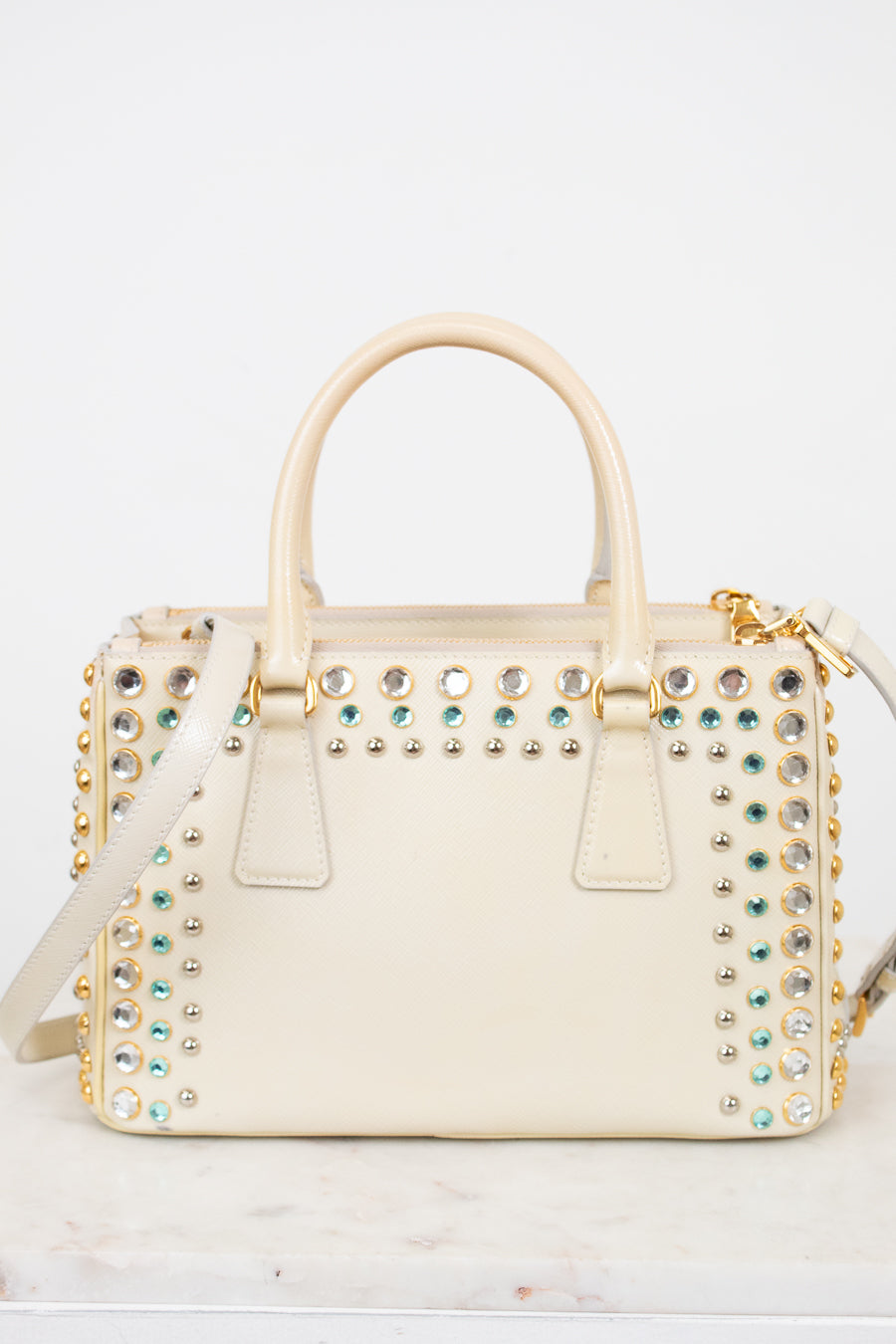 Cream-colored handbag with gold and multi-color gemstone embellishments on a light gray background