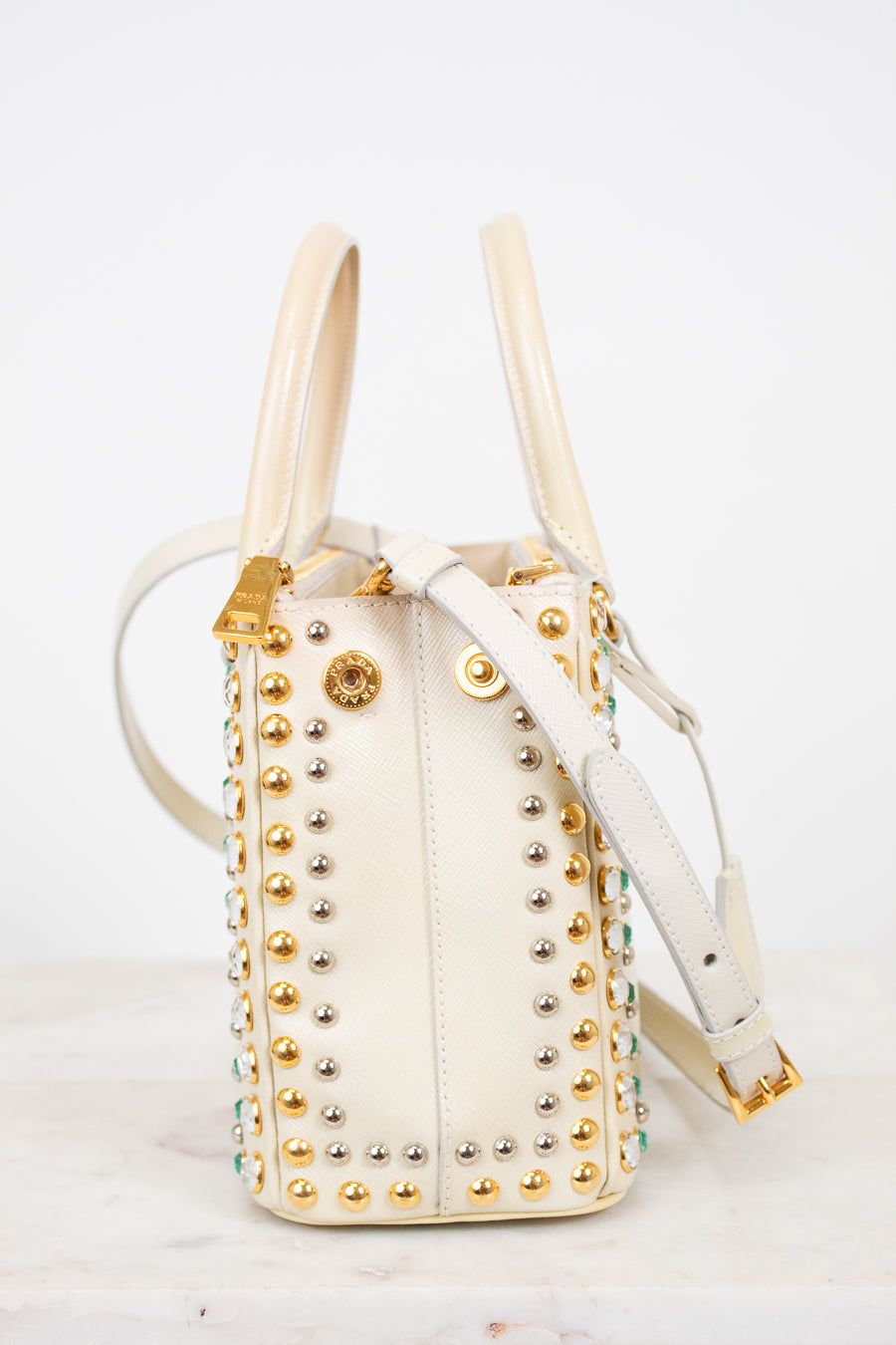 Cream handbag with gold studs and handles on a white background