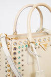 Beige handbag with decorative studs and gemstones on a white background