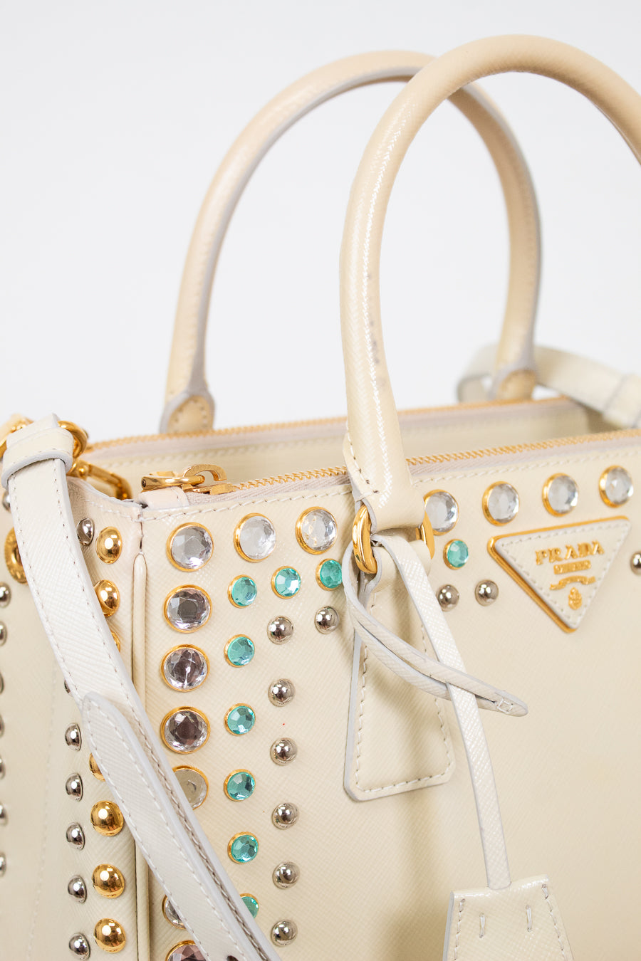 Beige handbag with decorative studs and gemstones on a white background