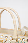 Close-up of strap on beige handbag with decorative stones on a light gray background showing stain on handle 